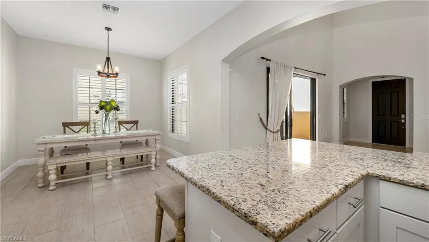 Kitchen featuring white cabinets, light stone counters, arched walkways, and a kitchen bar