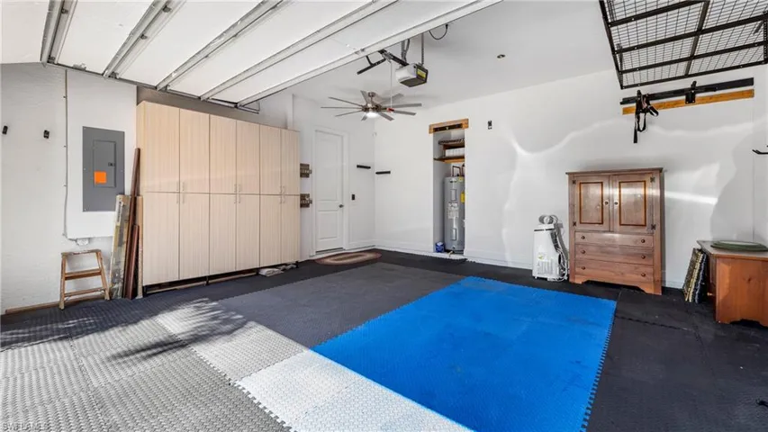 Garage with electric panel, a ceiling fan, electric water heater, and a garage door opener