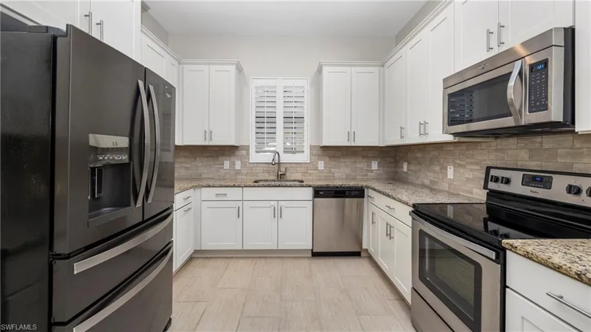 Kitchen featuring stainless steel appliances, white cabinetry, light stone counters, and backsplash