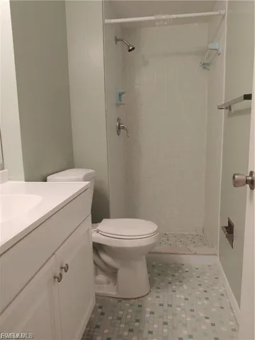 White vanity with a single basin sink, mosaic tile flooring, and a shower stall with a tiled surround