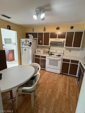 Kitchen featuring white appliances, extractor fan, dark brown cabinetry, and light countertops