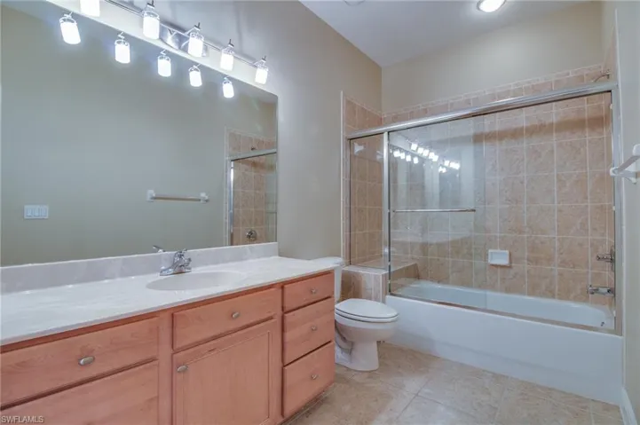 Full bath featuring bath / shower combo with glass door, vanity, and light tile patterned flooring