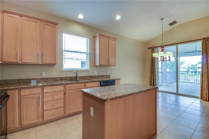 Kitchen featuring a center island, light tile patterned flooring, dark stone countertops, pendant lighting, and vaulted ceiling