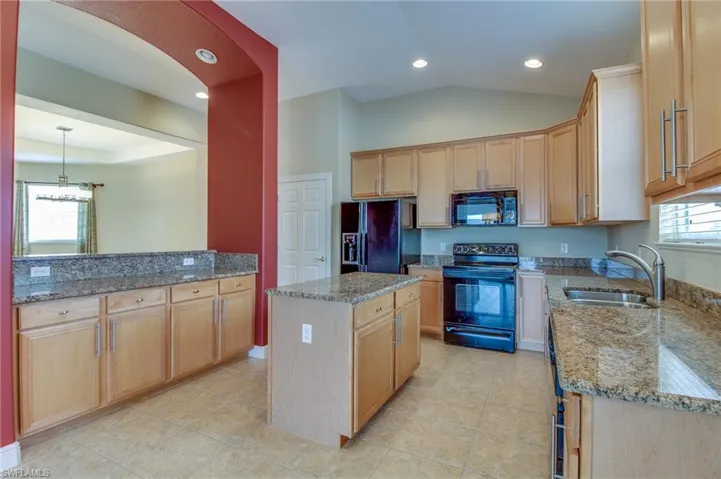 Kitchen with black appliances, light stone counters, a kitchen island, light brown cabinetry, and recessed lighting
