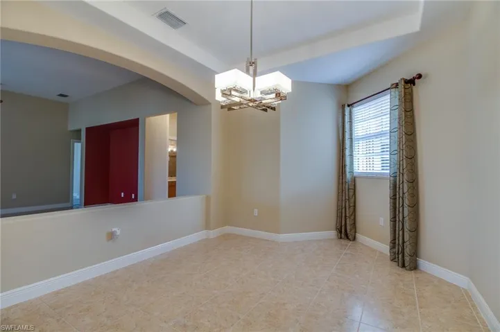 Empty room featuring arched walkways, a chandelier, and light tile patterned floors