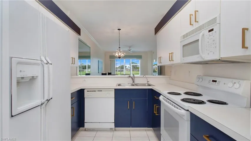 Kitchen featuring white appliances, light tile patterned floors, blue cabinets, pendant lighting, and sink