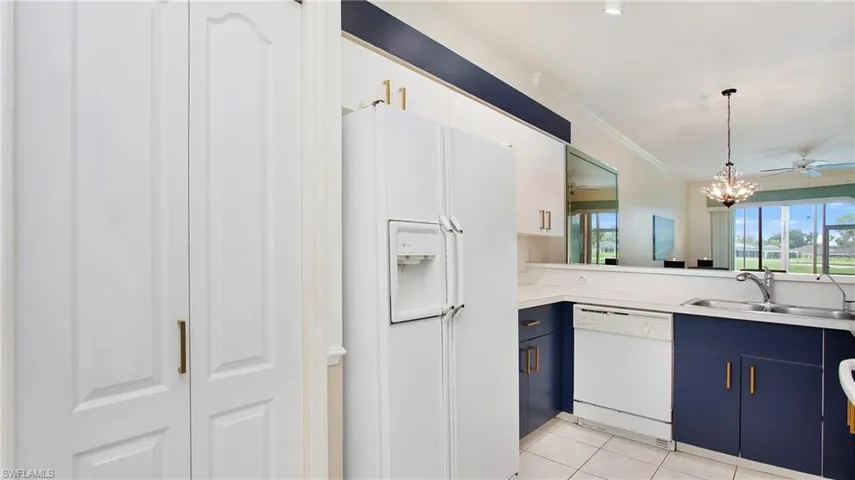 Kitchen with blue cabinets, ceiling fan with notable chandelier, pendant lighting, white appliances, and light tile patterned floors