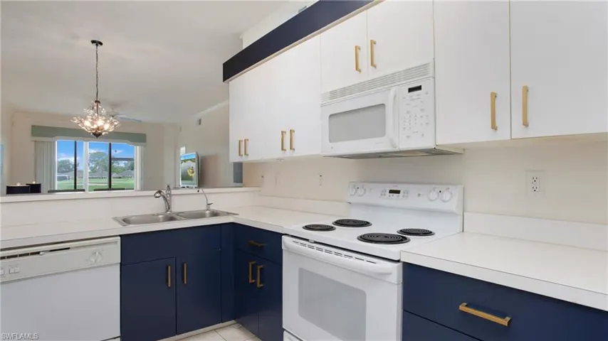Kitchen with white appliances, white cabinets, sink, hanging light fixtures, and blue cabinetry