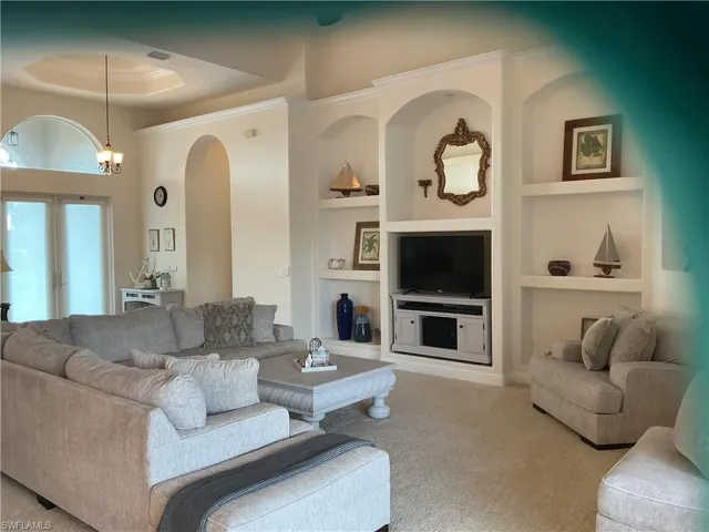 Carpeted living area featuring built in features, french doors, and a raised ceiling