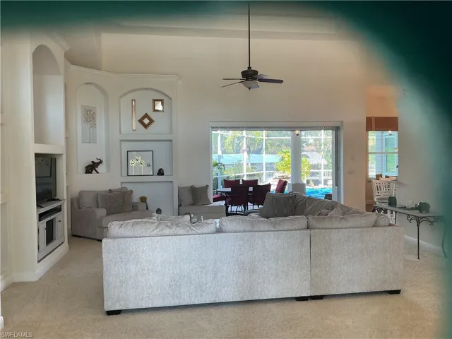Living area with a ceiling fan, a high ceiling, light colored carpet, and built in features