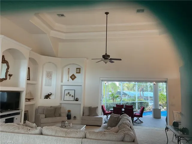 Living room with built in features, ceiling fan, crown molding, a raised ceiling, and a sunroom