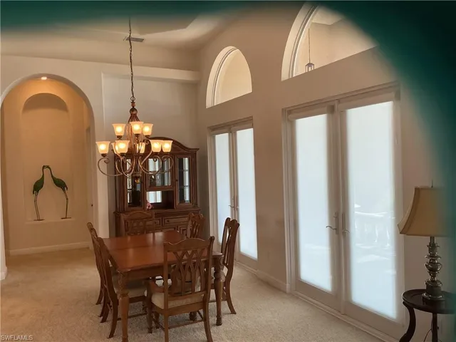 Dining area with light carpet, suspended lighting, and a high ceiling