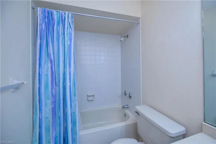 Bathroom with shower / bathtub combination with curtain and toilet