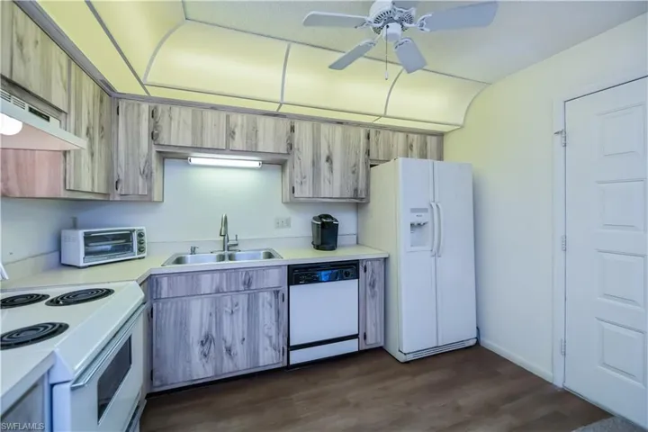 Kitchen featuring white appliances, light countertops, dark wood-type flooring, a ceiling fan, and under cabinet range hood