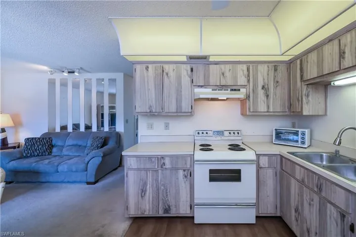 Kitchen featuring white electric range, open floor plan, light countertops, under cabinet range hood, and a textured ceiling