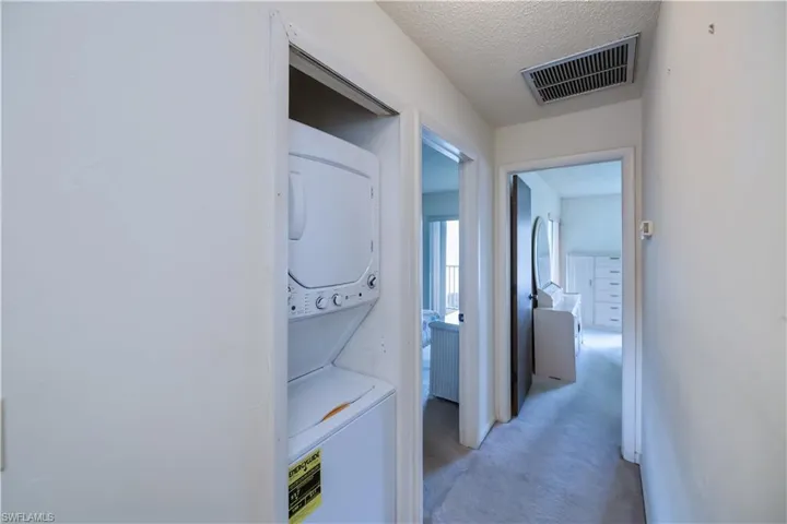 Corridor with carpet floors, stacked washer / drying machine, and a textured ceiling