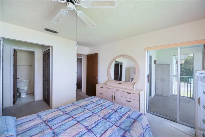 Carpeted bedroom with a textured ceiling, connected bathroom, ceiling fan, and access to exterior