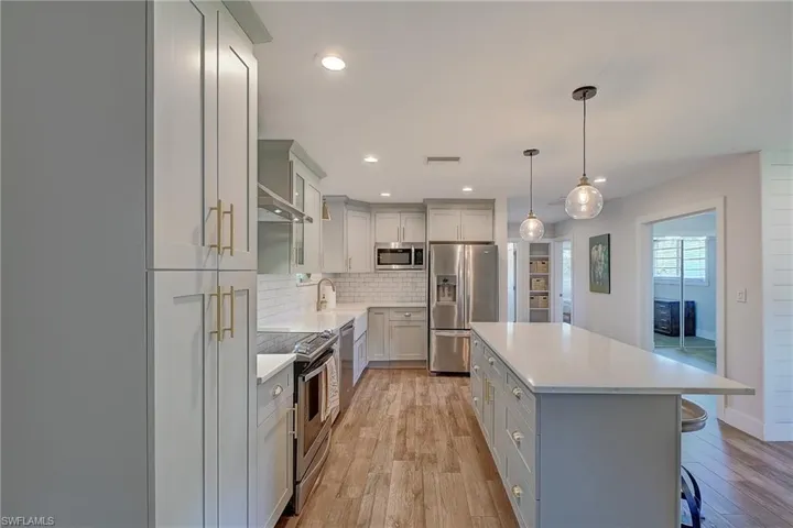 Kitchen with decorative backsplash, light hardwood / wood-style flooring, stainless steel appliances, a kitchen island, and a breakfast bar area