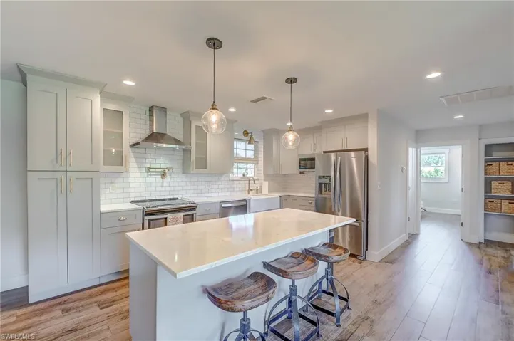 Kitchen featuring decorative backsplash, appliances with stainless steel finishes, wall chimney range hood, light wood-type flooring, and a kitchen island