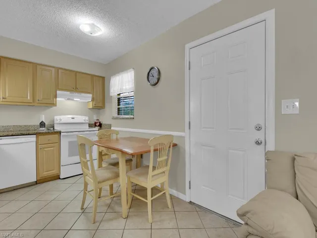 Kitchen with light brown cabinets, white appliances, stone countertops, a textured ceiling, and light tile patterned floors