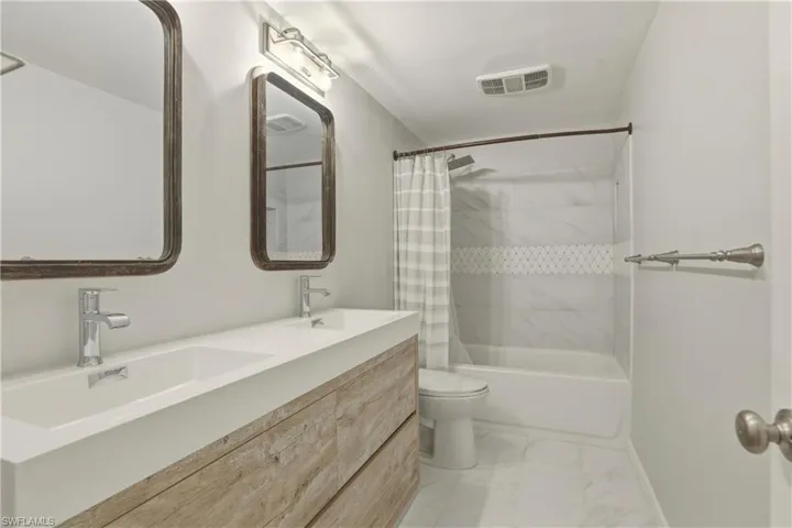 Full bath with shower / bath combination with curtain, double vanity, and light marble finish flooring