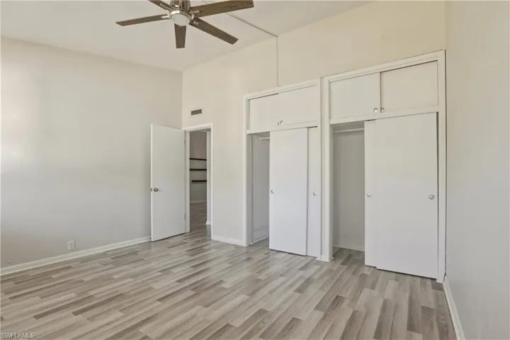 Unfurnished bedroom with two closets, light wood-style floors, a ceiling fan, and lofted ceiling