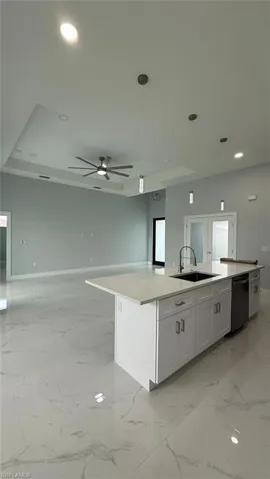 Kitchen with pendant lighting, recessed lighting, a kitchen island with sink, light stone counters, and white cabinetry