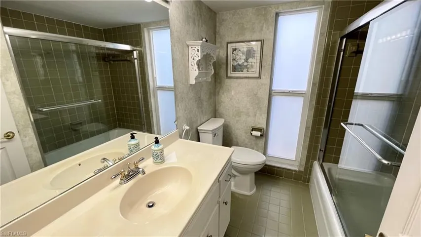 Full bath with vanity, bath / shower combo with glass door, and dark tile patterned floors