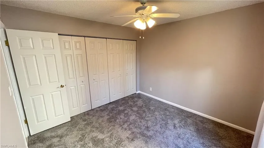 Unfurnished bedroom featuring new carpet, a closet, a textured ceiling, and ceiling fan