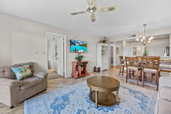 Tiled living room featuring ceiling fan with notable chandelier and a textured ceiling