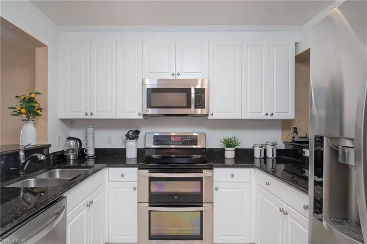 Kitchen with stainless steel appliances, dark stone counters, and white cabinetry