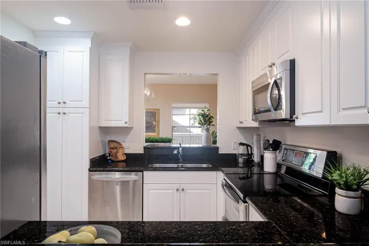 Kitchen featuring appliances with stainless steel finishes, white cabinetry, dark stone counters, recessed lighting, and a chandelier