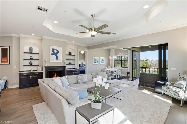 Living area with wood finished floors, a tray ceiling, a lit fireplace, a ceiling fan, and crown molding