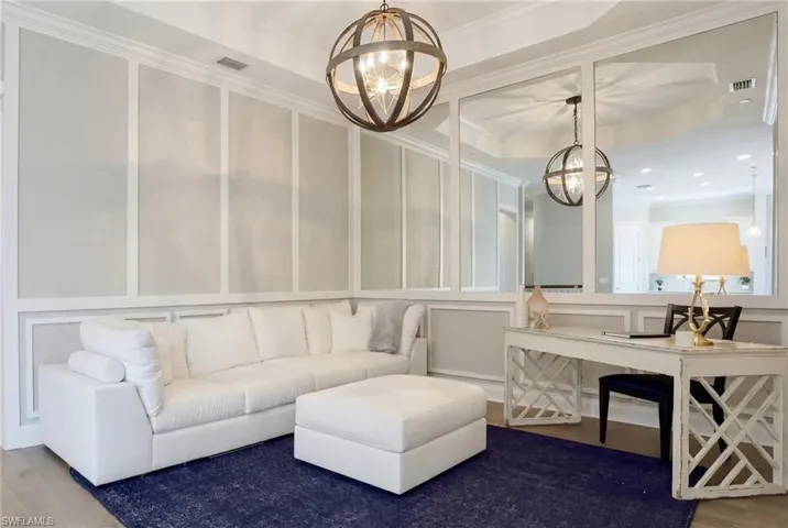 Living area featuring a decorative wall, a raised ceiling, crown molding, wood finished floors, and a chandelier