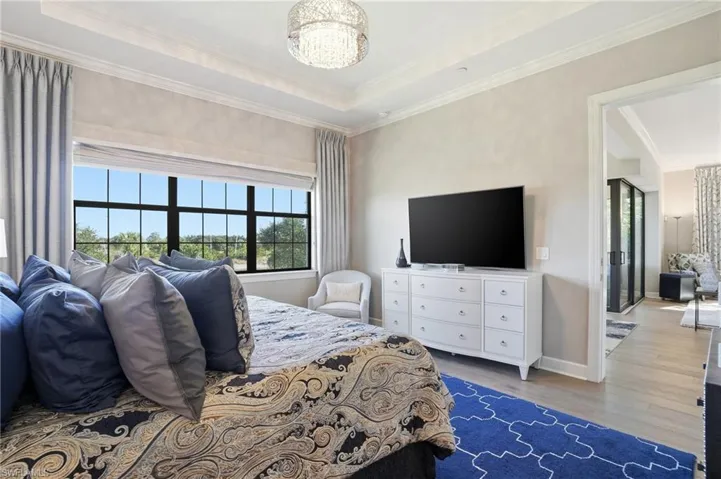 Bedroom featuring wood finished floors, a raised ceiling, crown molding, and a chandelier