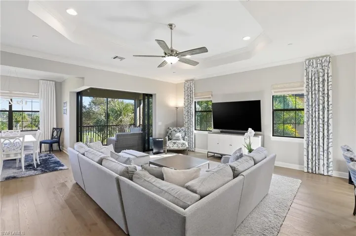 Living room with a raised ceiling, a ceiling fan, ornamental molding, wood finished floors, and recessed lighting