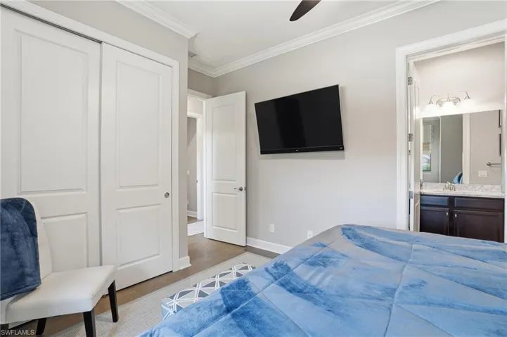 Bedroom featuring ornamental molding, ensuite bathroom, a closet, wood finished floors, and ceiling fan