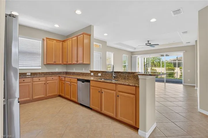 Kitchen featuring a raised ceiling, dark stone counters, appliances with stainless steel finishes, light tile patterned floors, and a peninsula