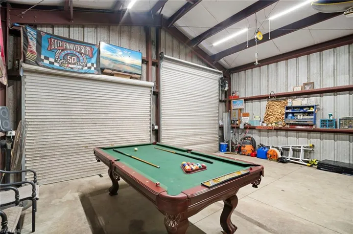 Game room featuring metal wall, a garage, concrete floors, billiards, and lofted ceiling