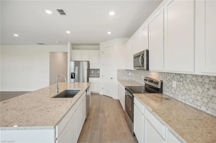 Kitchen with a center island with sink, appliances with stainless steel finishes, sink, and white cabinetry