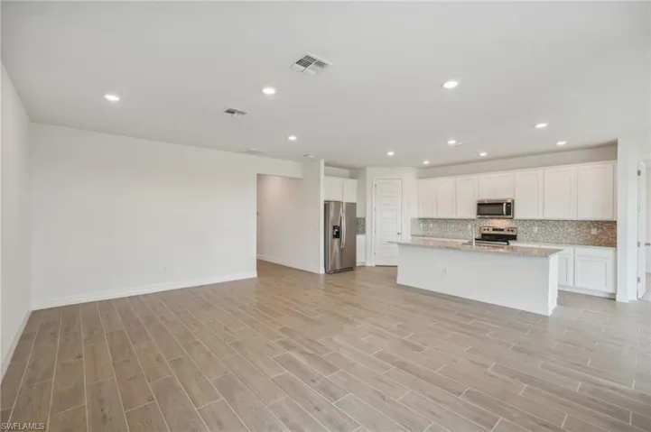 Kitchen with white cabinets, an island with sink, appliances with stainless steel finishes, light wood-type flooring, and decorative backsplash