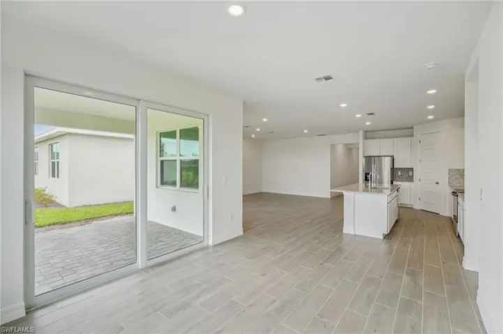 Kitchen featuring light wood-type flooring, a healthy amount of sunlight, a kitchen island with sink, and stainless steel fridge with ice dispenser