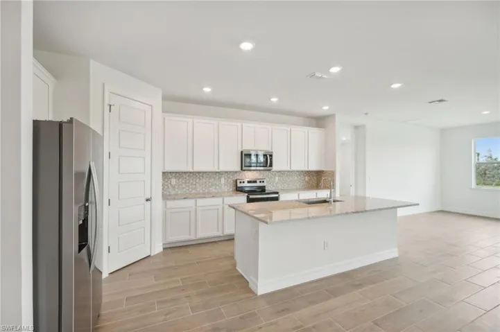 Kitchen with appliances with stainless steel finishes, light hardwood / wood-style floors, white cabinets, a kitchen island with sink, and sink