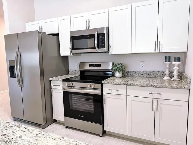 Kitchen featuring white shaker-style cabinetry, granite countertops, and stainless steel appliances including a refrigerator, range, and microwave