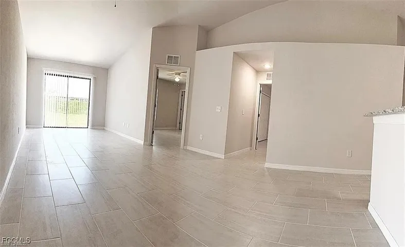 Expansive living area featuring light-toned tile flooring, vaulted ceilings, and neutral wall tones
