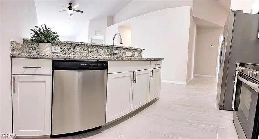 Kitchen featuring white shaker-style cabinetry, a stainless steel dishwasher, a gooseneck faucet, light-toned tile flooring, and a stone countertop with a matching backsplash