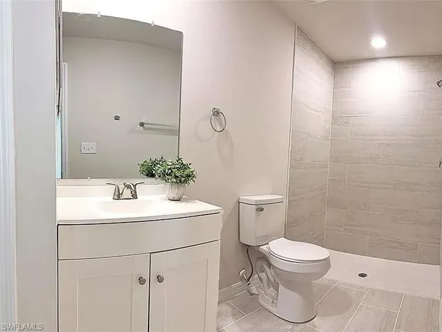 Bathroom featuring a walk-in shower with large format tile, a vanity with a white countertop and integrated sink, a contemporary toilet, and light-tone tile flooring