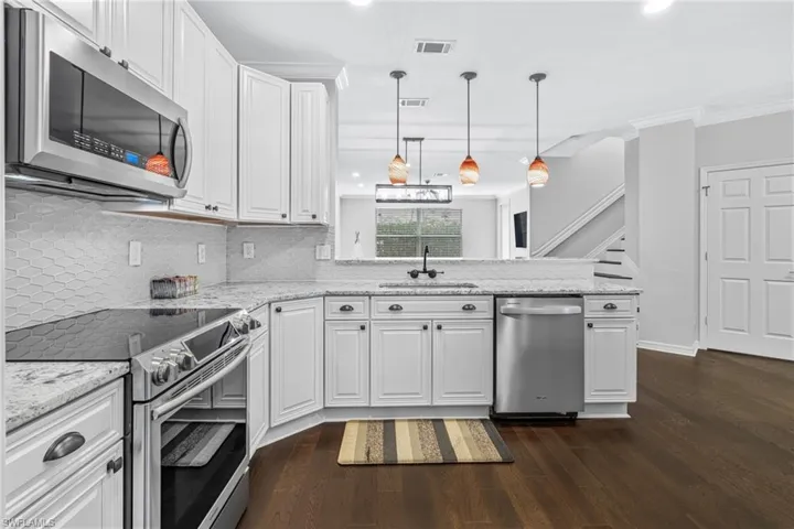 Kitchen featuring sink, pendant lighting, stainless steel appliances, decorative backsplash, and white cabinets