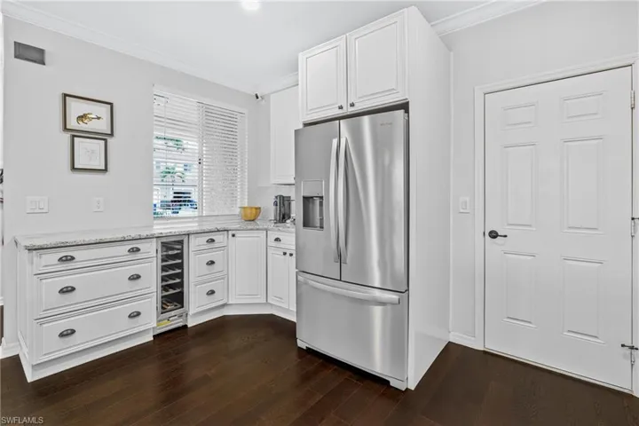 Kitchen featuring stainless steel refrigerator with ice dispenser, beverage cooler, light stone counters, and white cabinets