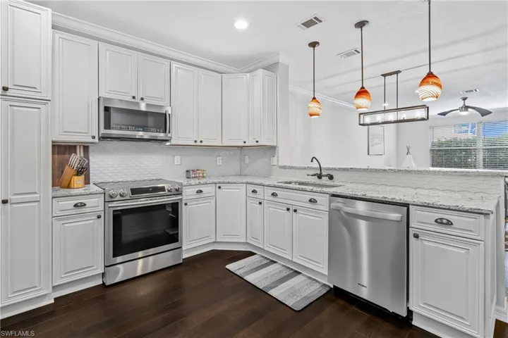 Kitchen with decorative light fixtures, tasteful backsplash, white cabinetry, sink, and stainless steel appliances